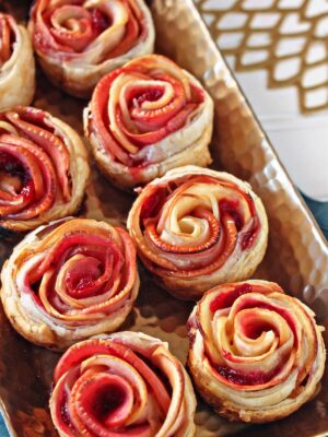 Baked Puff Pastry Apple Roses on a baking tray on a teal napkin.