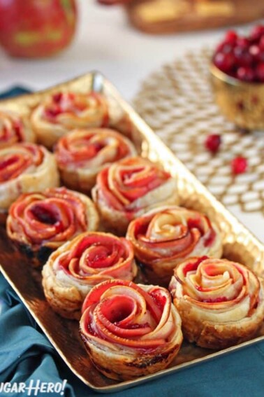 Baked Apple Cranberry Gouda Puff Pastry Roses on a baking tray with cranberries and apples in the background.