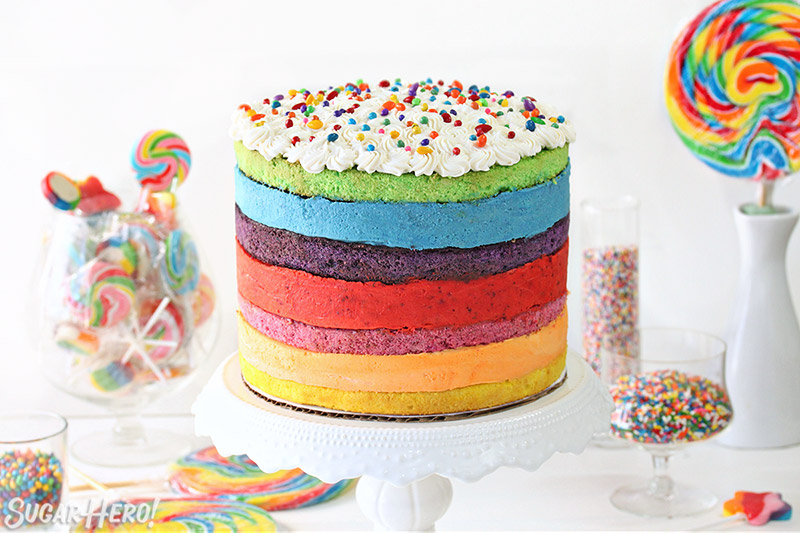 Rainbow Mousse Cake on a white cake stand with colorful candy surrounding it.
