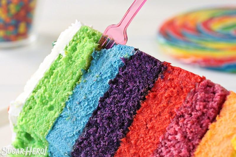 Rainbow Mousse Cake | From SugarHero.com Close-up of a slice of Rainbow Mousse Cake with a pink fork sticking out of the top.