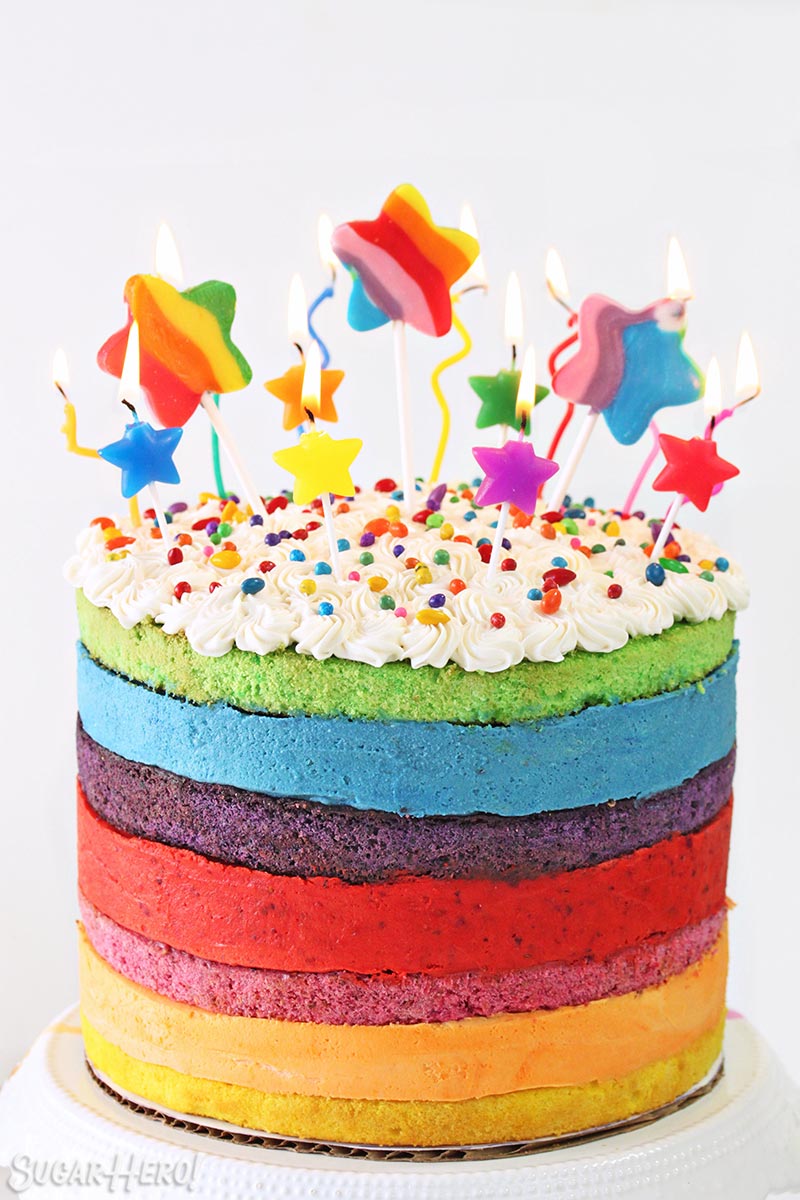 Rainbow Mousse Cake with star-shaped candles burning on top.