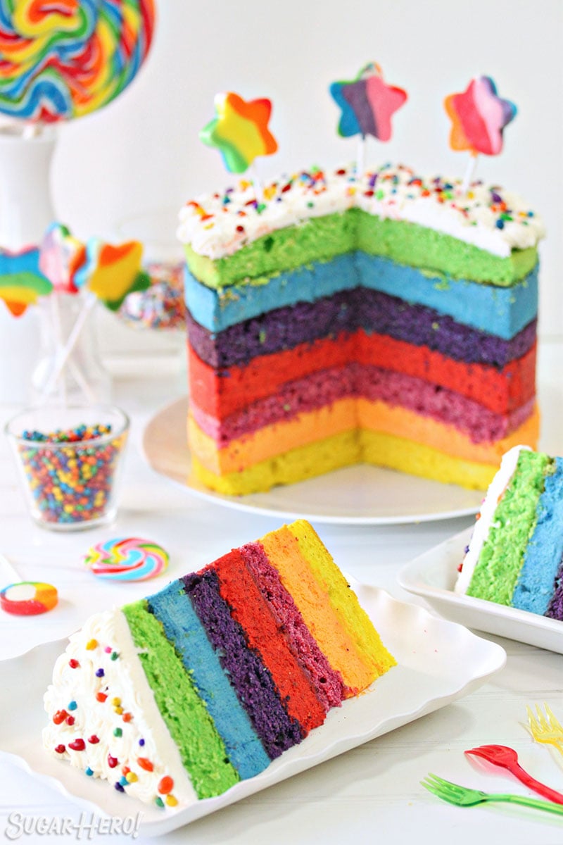 Rainbow Mousse Cake with several slices cut out of it, on fluted plates in front of the cake.