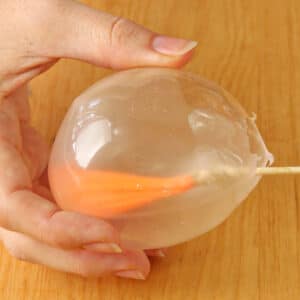 Hand removing a water balloon from the inside of a gelatin globe.