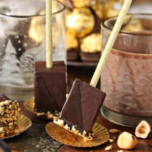 2 pieces of Hazelnut Hot Chocolate On A Stick next to holiday glasses.