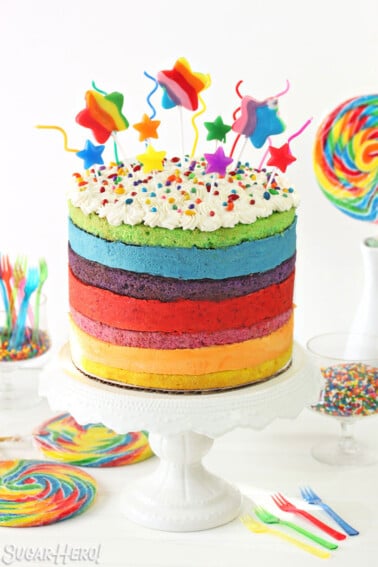 Rainbow Mousse Cake on a white cake stand with colorful candies surrounding it.