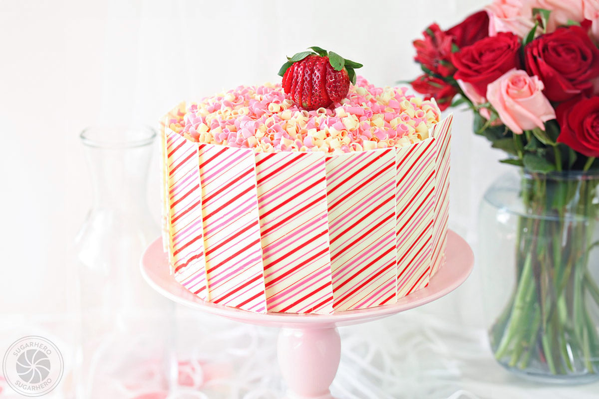 Strawberries and Cream Layer Cake - cake with pink and white striped white chocolate panels and pink and white chocolate curls on top | From SugarHero.com