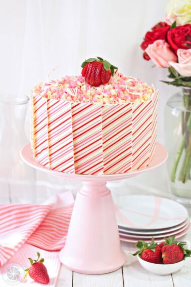 Layer cake covered with white chocolate panels on a pink cake stand.
