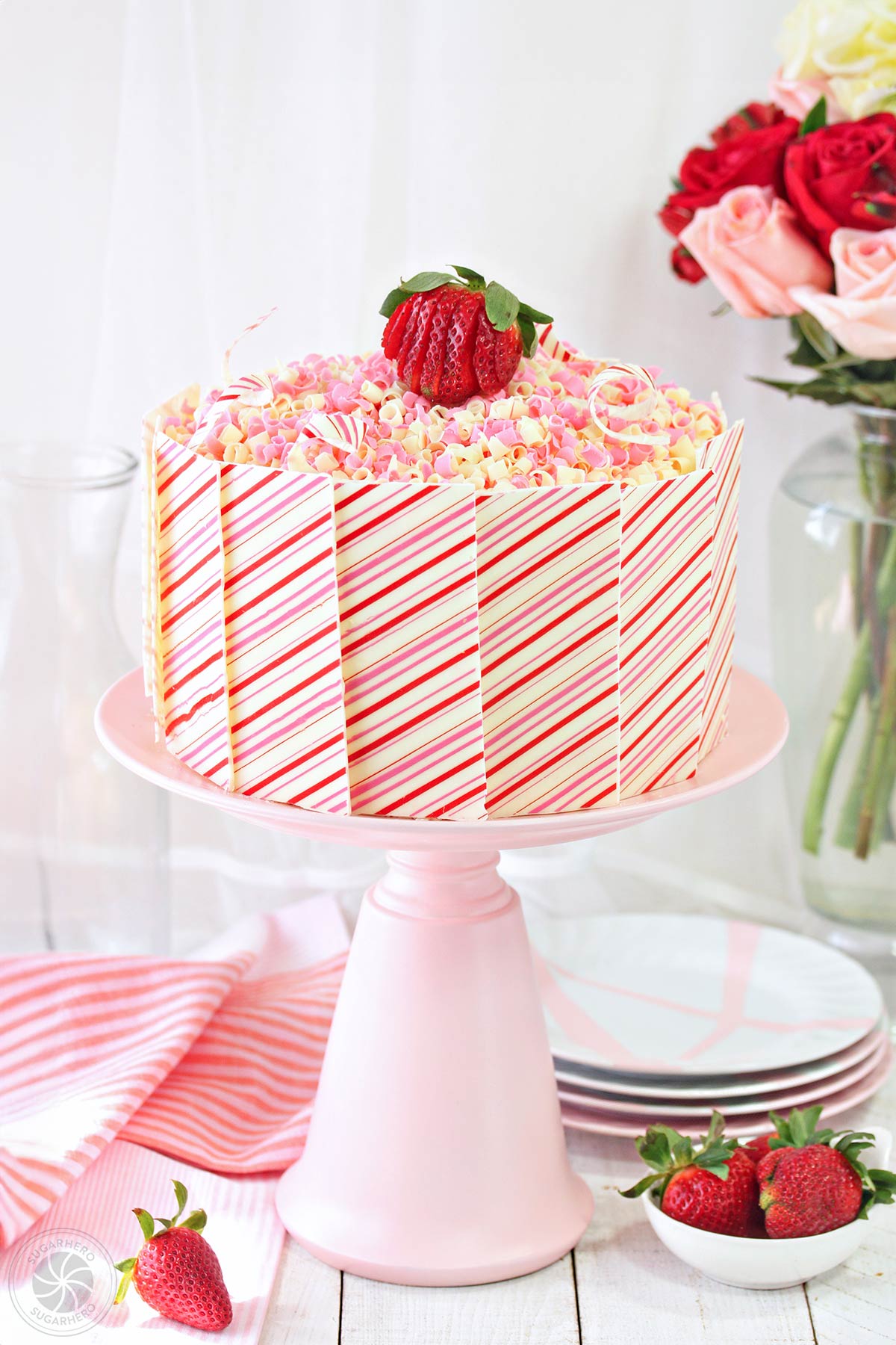 Strawberries and Cream Layer Cake - with moist strawberry cake, fresh berries, and whipped cream! | From SugarHero.com Strawberries and Cream Layer Cake - cake covered in pink and white striped chocolate panels, on a pink cake stand | From SugarHero.com