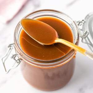 Top view of a jar of Caramel sauce with a spoon holding a spoonful of sauce.