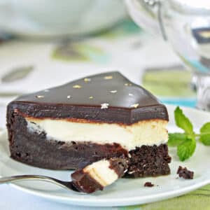 A slice of Peppermint Patty Flourless Chocolate Cake on a small white plate next to a fork holding a bite of cake.