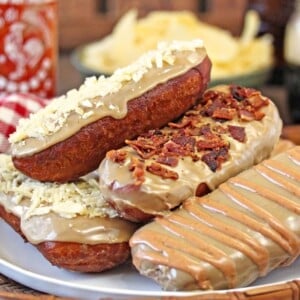 A stack of Bronuts on a white plate covered in toppings of potato chips, bacon and sriracha glaze.