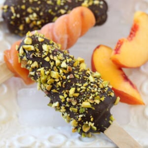 Close up of a chocolate and pistachio covered Peach Passion Pop with more pops in the background.