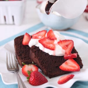 Close up of Chocolate Pound Cake on a white plate with strawberries and whipped cream.