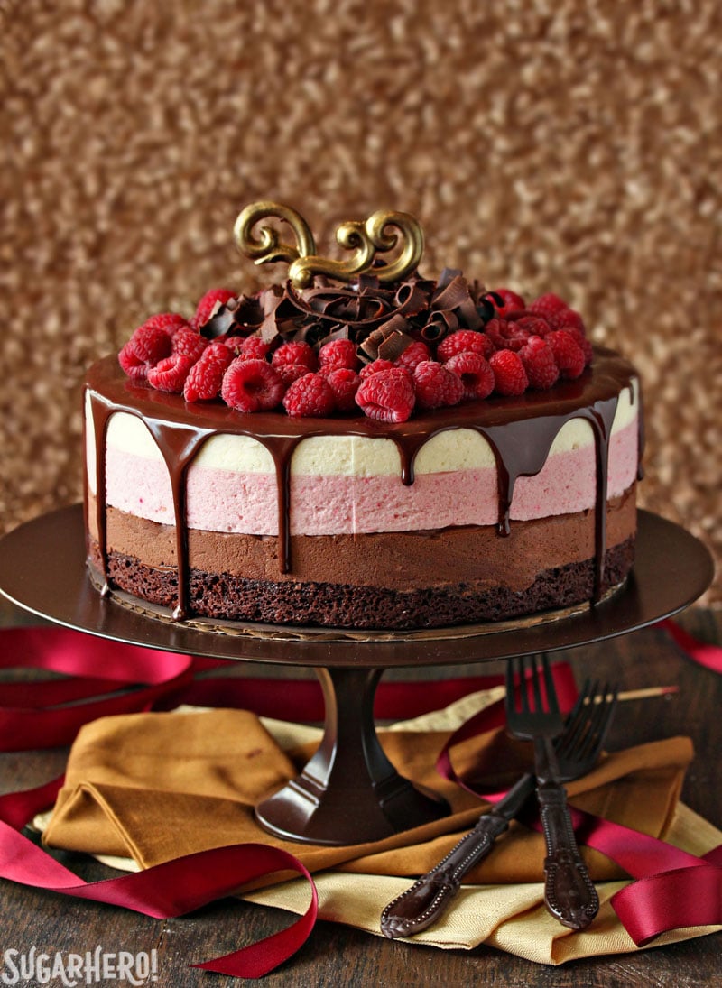 This stunning Chocolate Raspberry Mousse Cake has a moist, fudgy brownie base, three layers of light mousse—chocolate, raspberry, and vanilla, and then a glossy topping of chocolate and a tangle of raspberries and chocolate curls on top. Perfect for any occasion! | From SugarHero.com Chocolate Raspberry Mousse Cake - A front view shot of mousse cake. | From SugarHero.com