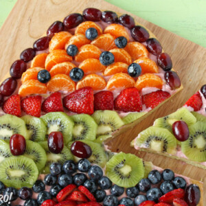 Easter Egg Fruit Pizza on a wooden cutting board with a slice removed