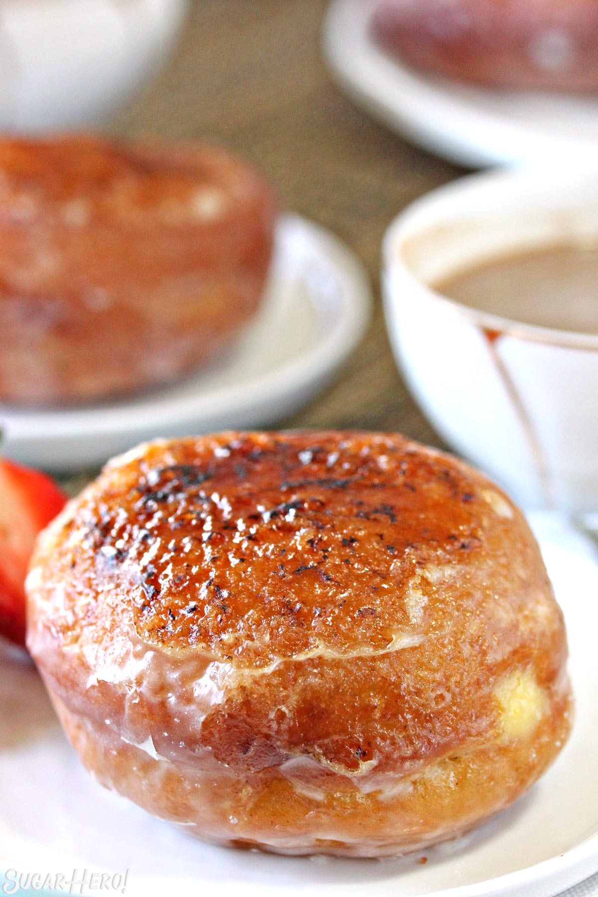 Two Crème Brûlée Donuts on white plates, with shiny caramelized sugar crusts on top.