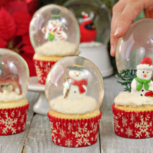 Four snow globe cupcakes with hand placing globe on the last cupcake.