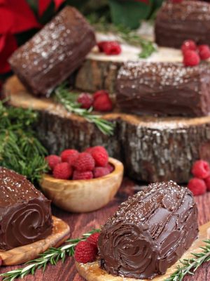 Mini Buche de Noel on a wooden surfaces with rosemary and raspberries.