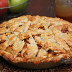 Golden brown crust of Salted Caramel Apple Pear Pie with apples and caramel in the background.
