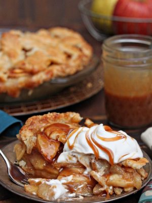 Slice of Salted Caramel Apple Pear Pie with whipped cream and caramel on top.