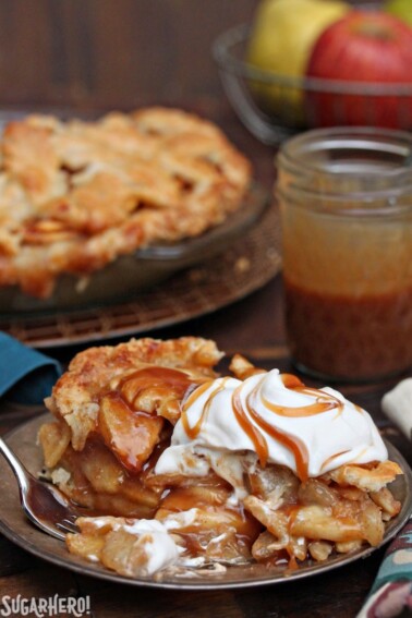 Slice of Salted Caramel Apple Pear Pie with whipped cream and caramel on top.