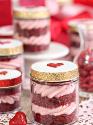 Red velvet cake in a jar with the lid on and multiple jars in the background.
