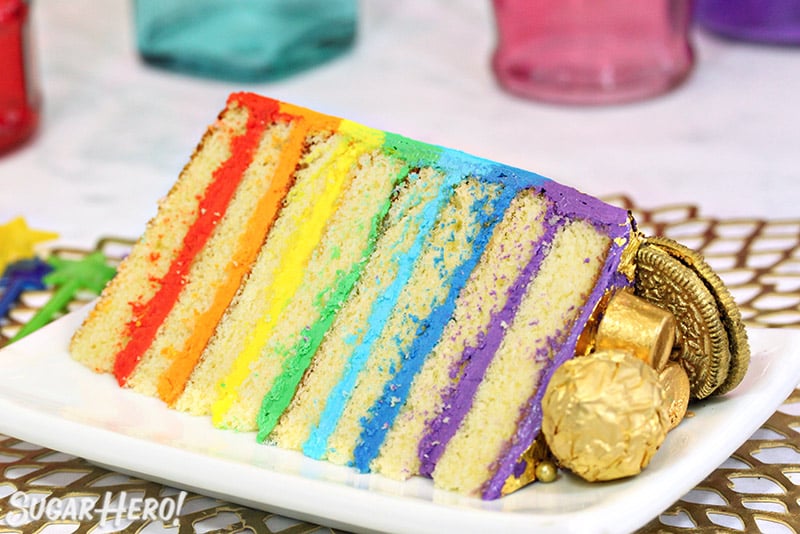 Close-up of a slice of rainbow cake on a white rectangular plate.