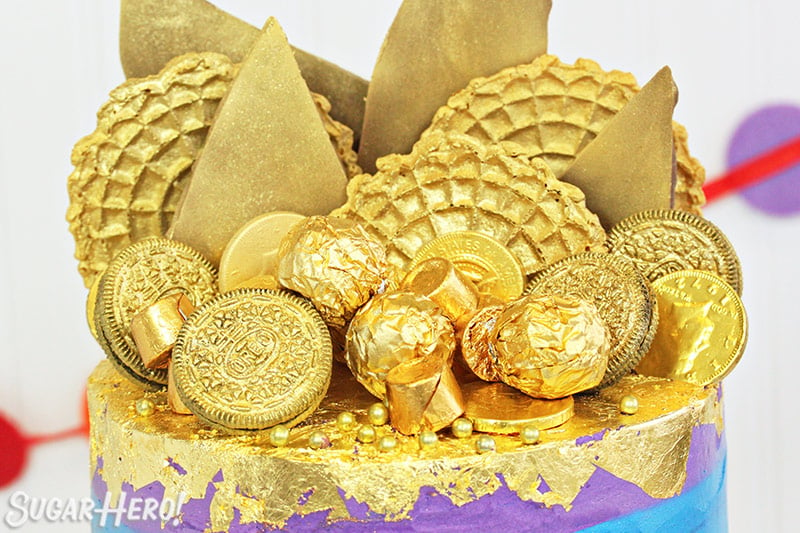 Close-up of the gold candies and embellishments on top of a rainbow cake.