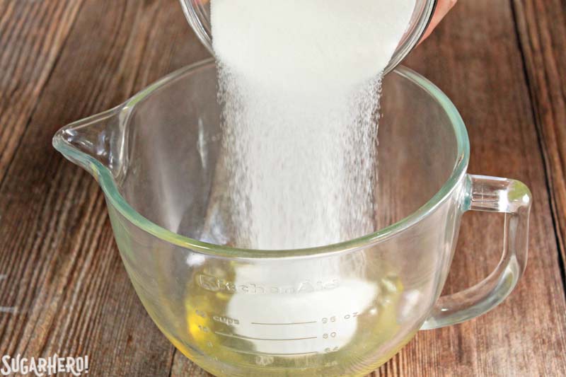 How to Make Swiss Meringue Buttercream - A photo of sugar being poured into the egg whites.  | From SugarHero.com