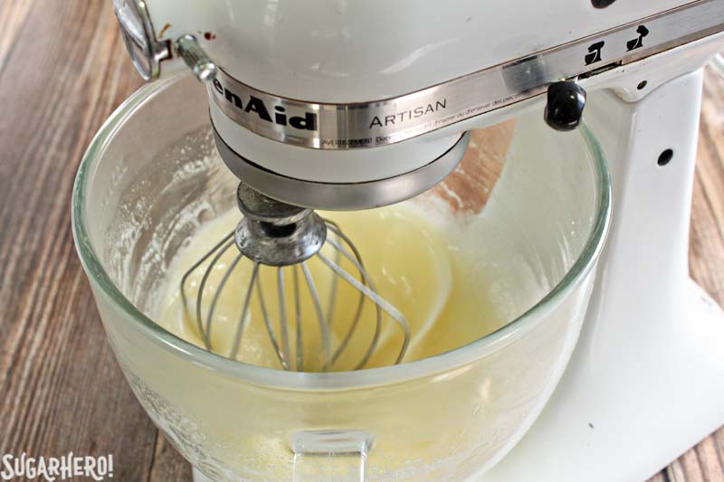 Swiss Meringue Buttercream is delicious, versatile, and the BEST frosting to use for layer cakes. Learn how to make it with this Swiss Meringue Buttercream recipe and photo tutorial! | From SugarHero.com How to Make Swiss Meringue Buttercream - A close up shot of the mixture being mixed in a stand mixer. | From SugarHero.com