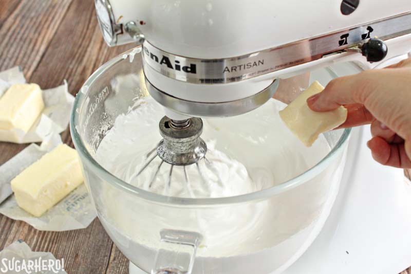 How to Make Swiss Meringue Buttercream -A shot showing the butter pieces being put into the mixture. | From SugarHero.com