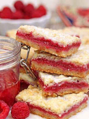 Stack of Raspberry Rhubarb Almond Bars next to a container of jam.