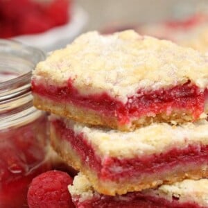 2 Raspberry Rhubarb Almond Bars next to a container of jam.