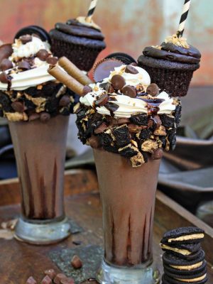 2 Epic Chocolate Peanut Butter Milkshakes on a counter next to a stack of cookies.