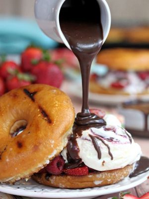 Chocolate being drizzled from a small white pitcher onto a Doughnut Strawberry Shortcake.