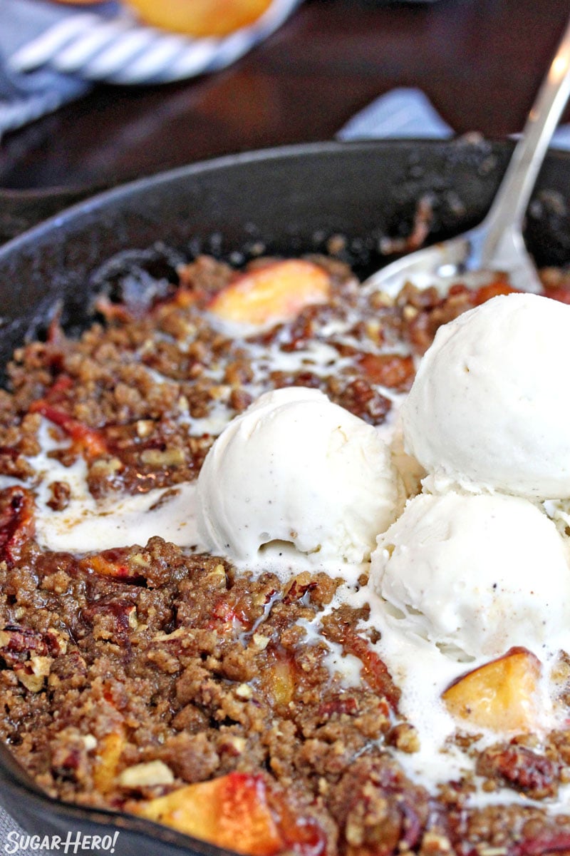 Cast iron skillet of peach crisp with scoops of vanilla ice cream on top