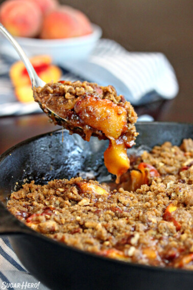 Spoon taking a big scoop of peach cobbler out of a cast iron skillet