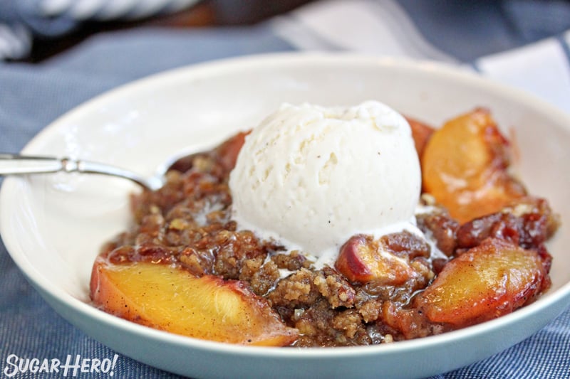 Bowl of peach crisp with a scoop of vanilla ice cream