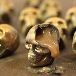 Close up of broken chocolate skill oozing caramel next to several full skulls.