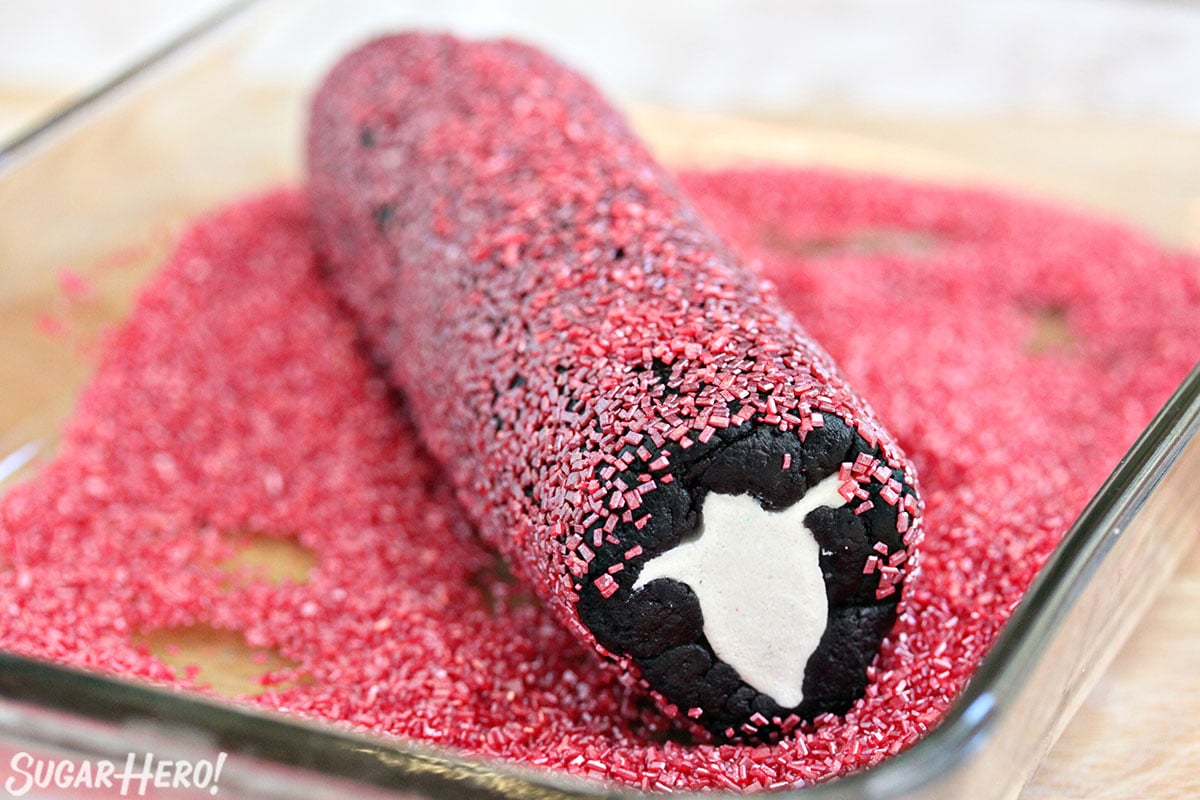 Ghost roll of Slice and Bake Halloween Cookies covered in pink sprinkles and sitting in a pan full of pink sprinkles.