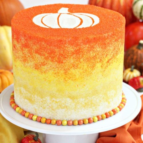 Stenciled Halloween Sprinkle Cake on a white cake stand with pumpkins in the background.