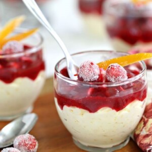 2 Orange Mousse Cups with Cranberry Sauce on a wooden table with a spoon inserted into the front cup.