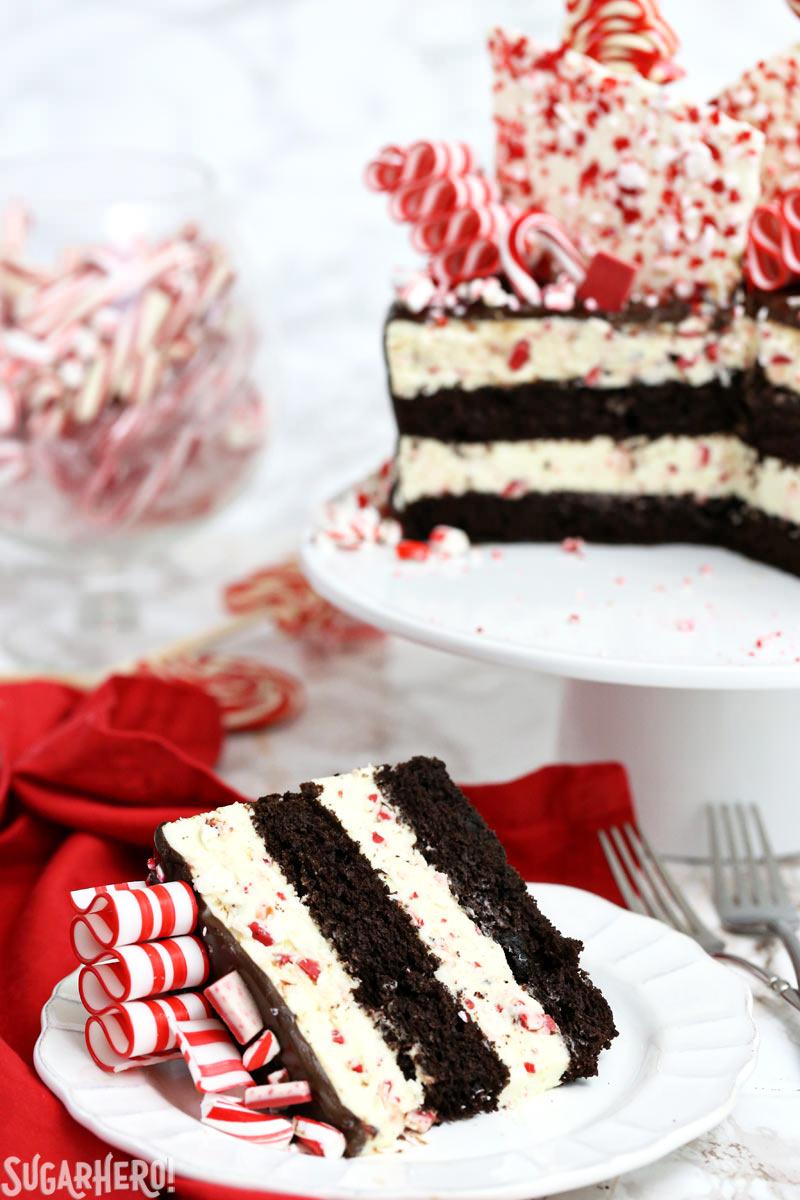 Slice of Candy Cane Mousse Cake on white plate with full cake on a cake stand behind it