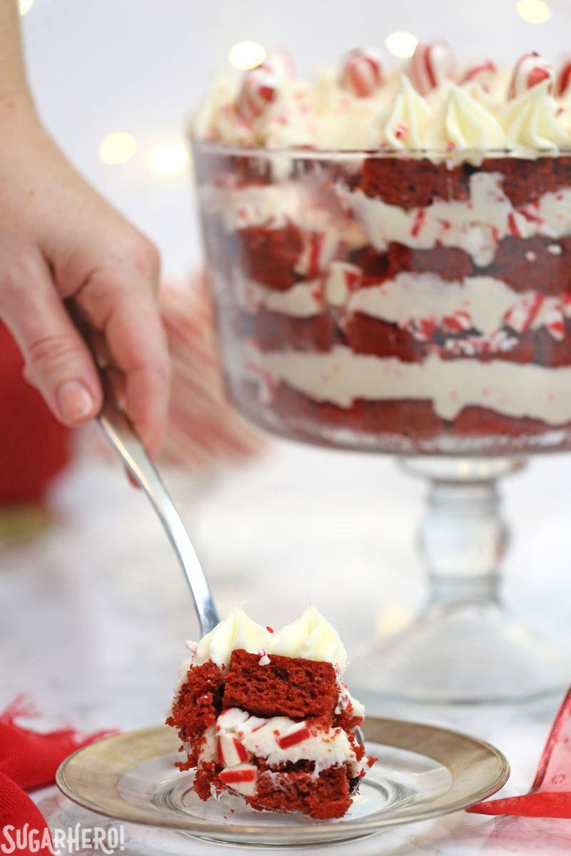 Hand serving a scoop of Red Velvet Trifle with the trifle bowl in the background