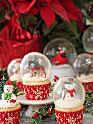 6 snow globe cupcakes with a poinsettia in the background.