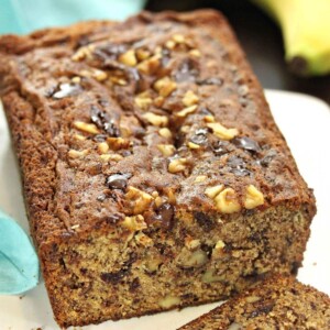 Loaf of Banana Bread with nuts and chocolate chunks, cut open on a white platter.
