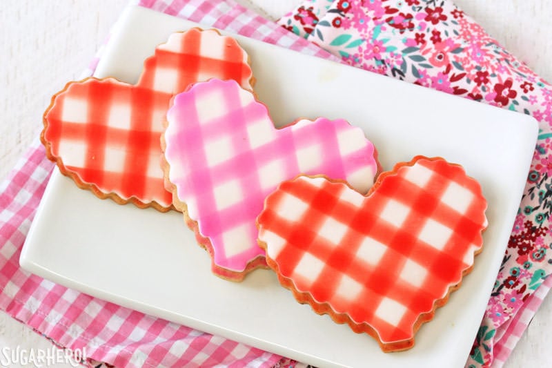 Brown Butter Heart Cookies - brown butter sugar cookies with pretty patterns for Valentine's Day! | From SugarHero.com Brown Butter Heart Cookies - three cookies with a gingham pattern on a white plate | From SugarHero.com
