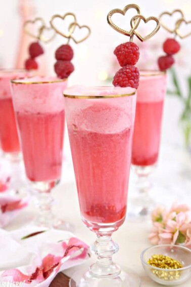 Tall gold-rimmed glasses with pink punch inside and a fresh raspberry garnish.