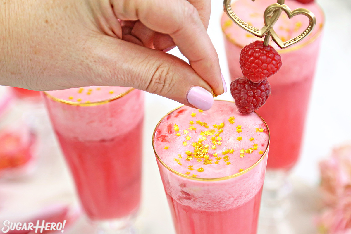 Hand sprinkling edible gold stars on top of a glass of pink Valentine's Day punch.