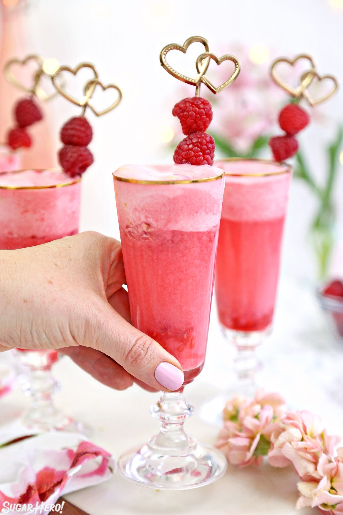 Hand lifting up a gold-rimmed glass filled with pink Valentine's Day punch.